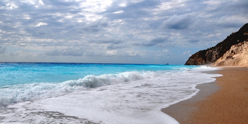 Scenic beach with turquoise waters, rocky hills, and a clear blue sky overhead.

