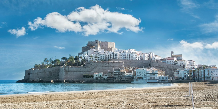 Peñíscola in Spain, with a sandy shoreline and distant traditional architectural buildings, one of the places to visit near Valencia.