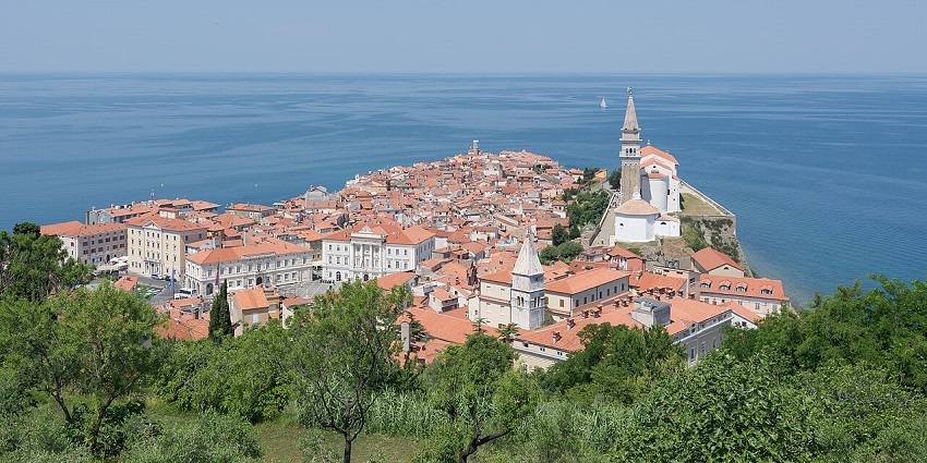 Scenic coastal town with terracotta rooftops and a church tower surrounded by calm blue sea, amongst the beautiful places to visiti near Ljubljana.