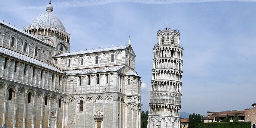 Famous leaning bell tower beside a historic cathedral with marble arches and green lawn.
