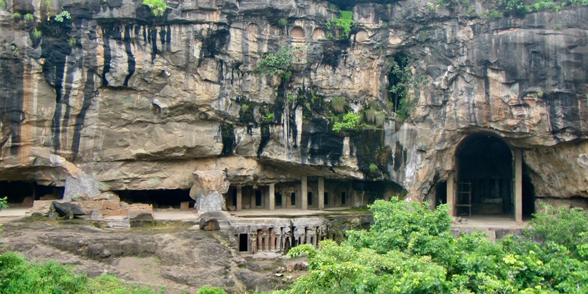 Pitalkhora Caves are carved into a rocky cliffside with multiple cave openings visible.