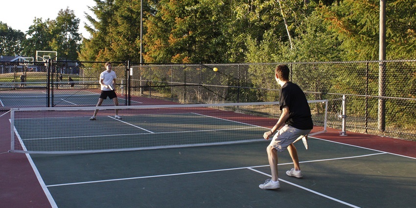 Two people playing pickleball with a pickleball playfield and a basketball court, one of the best things to do in Plymouth MN.