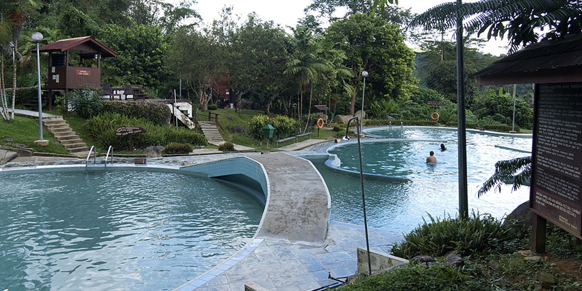 Poring hot springs with clear blue water, people in the water, sets of stairs, and greenery.