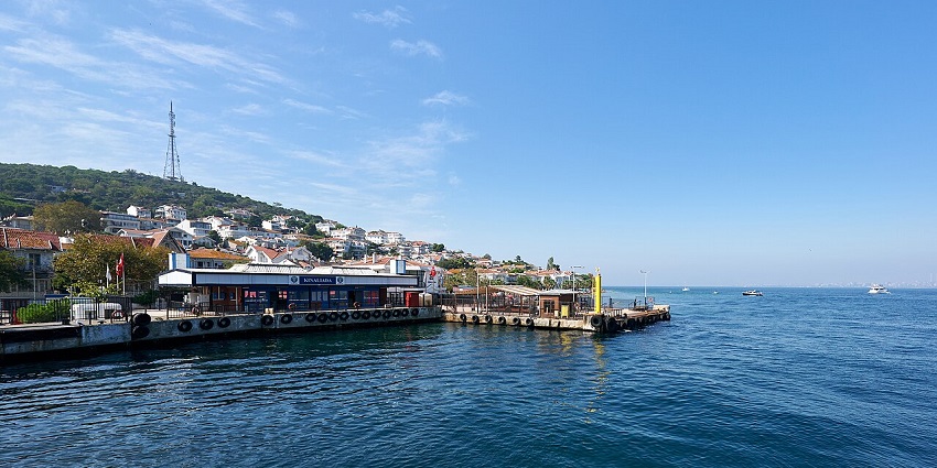 A peaceful coastal town with a ferry terminal, hillside houses, and boats on a calm sea, one of the top places to visit near Istanbul.