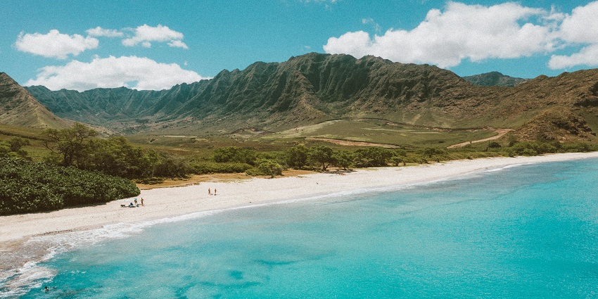Kaanapali beach with a sandy shoreline, clear waters, and is surrounded by lush green mountains.
