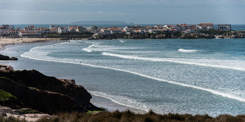 Praia dos Supertubos with sandy shoreline, incoming waves of the ocean and distant people.