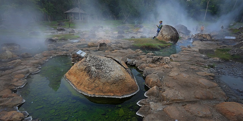 Clear natural hot springs surrounded by lush forest and rocks in a peaceful Pai setting.