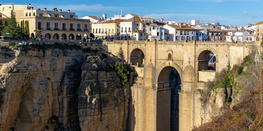 Old Spanish architectural bridge with traditional buildings and houses at a distance.
