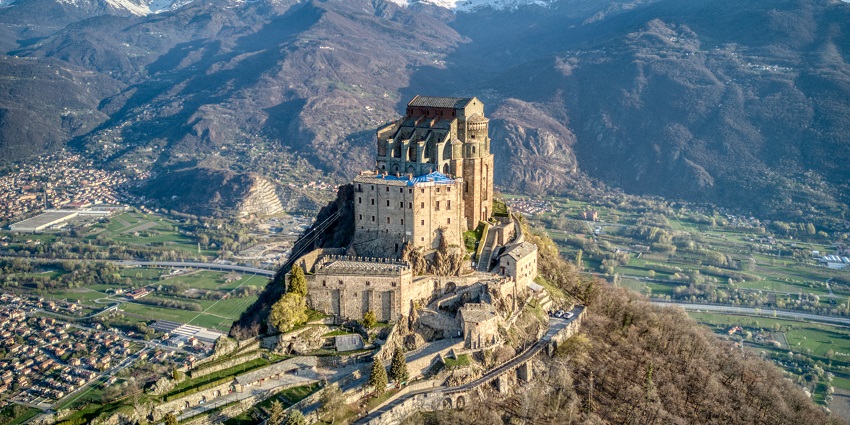 Sacra di San Michele with an old medieval castle on top of the mountain and green hills.