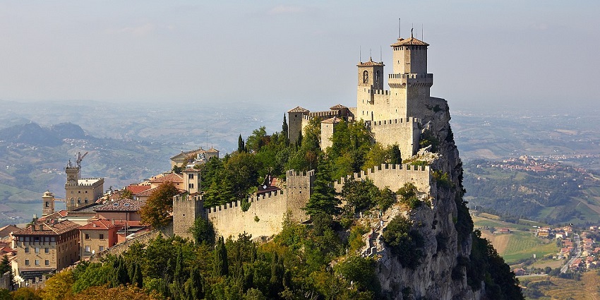 Guaita Fortress stands on rocky Monte Titano in San Marino, surrounded by mist and hills.