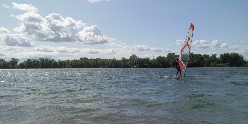 Shining lake with distant trees, water skiing, and one person yachting under cloudy sky.