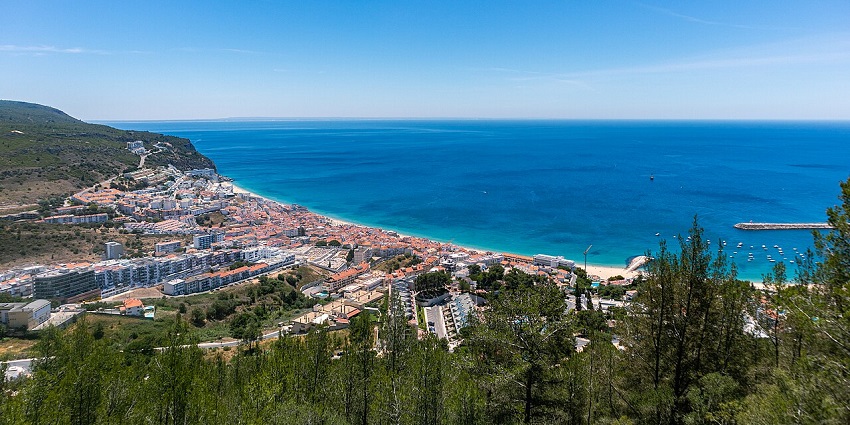 Coastal town with white buildings and red roofs nestled by the turquoise sea under a blue sky.