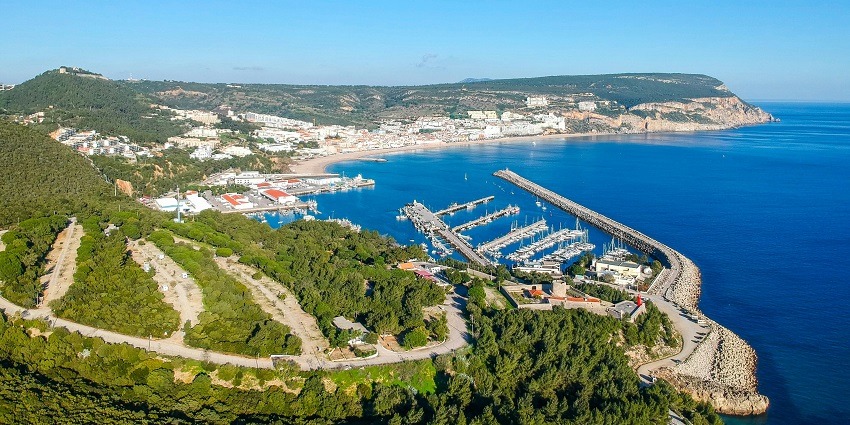 Lush green hills and calm sea waters surround Setúbal, Portugal, showcasing natural beauty.