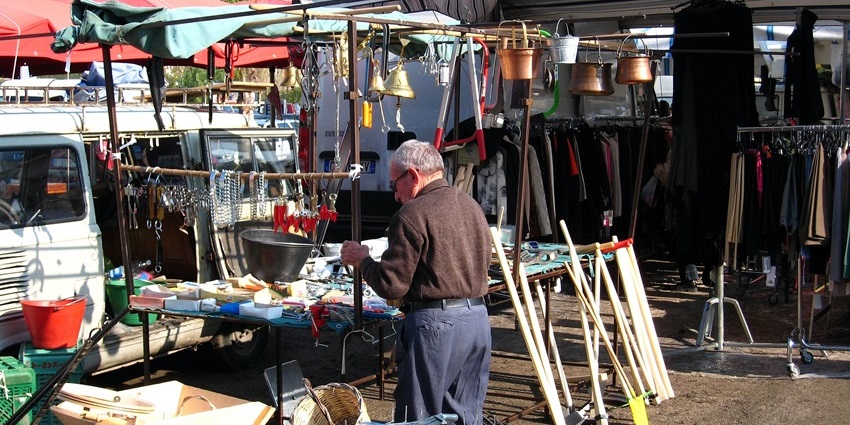 Open-air market stall in Maiori, Italy with tools, cookware, and clothing under tents.