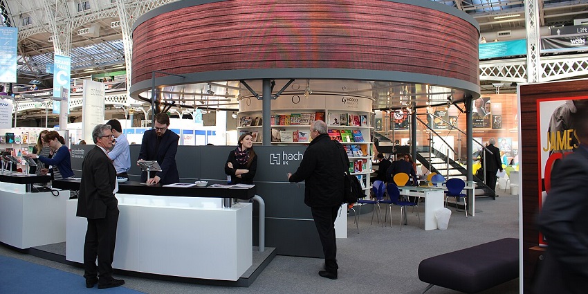 Modern indoor book fair booth with people interacting, bookshelves, and a circular deck.
