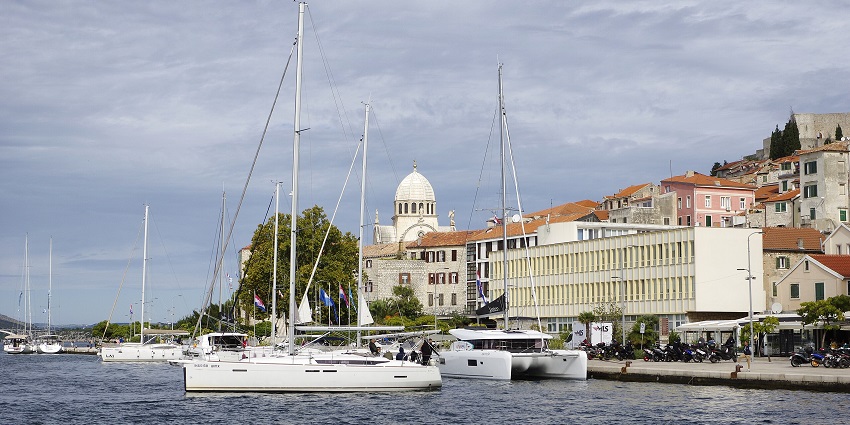 Šibenik in Croatia with multiple white boats on the harbour and buildings at a distance.
