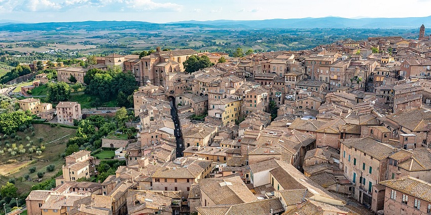 Aerial view of a historic town with terracotta rooftops surrounded by rolling green hills, one of the places to visit near Florence.
