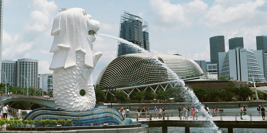 Merlion statue at Orchard Spring Lane in Singapore with city buildings and palm trees nearby.
