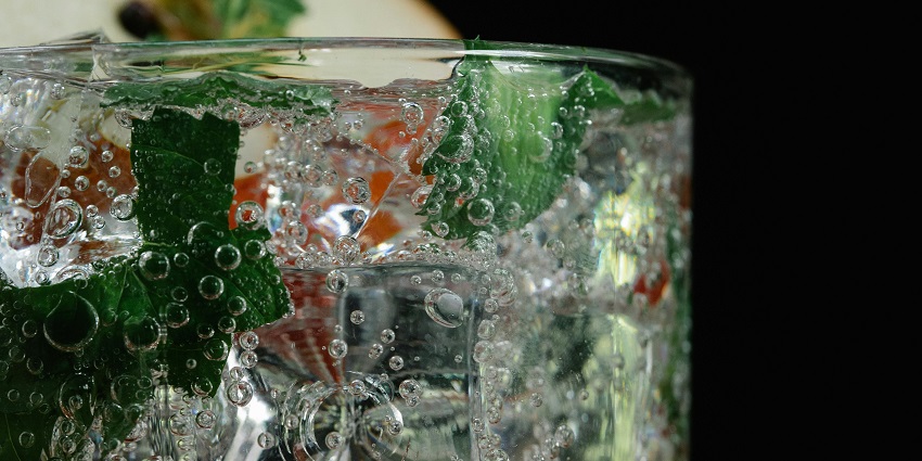 Sparkling water with ice and mint leaves bubbling up inside a clear cup made of glass.