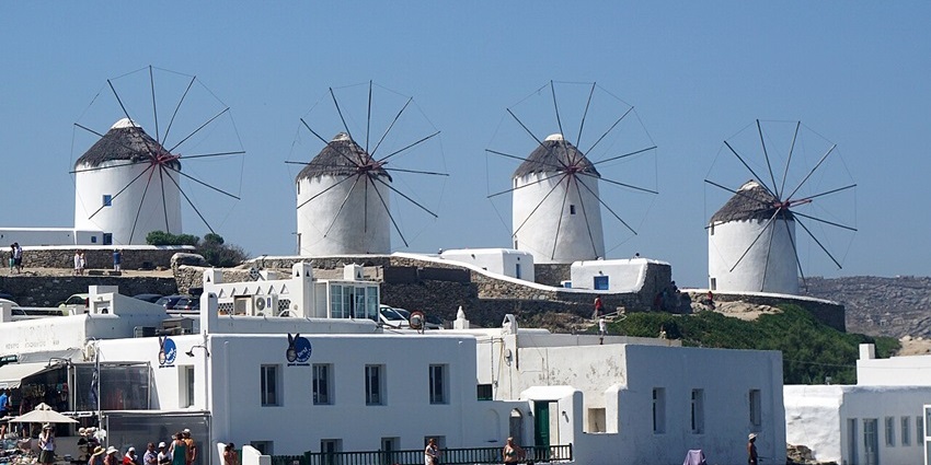 Iconic white windmills stand tall by the sea under a clear blue sky.
