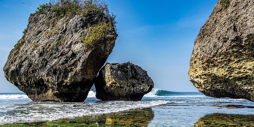 Thomas beach in Pecatu with a clear water body of the sea, algae under the water and big rocks.
