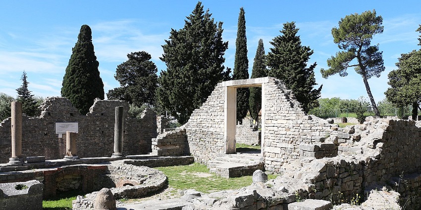 Solin in Croatia with old ruined architecture, broken walls, a gateway, and tall green trees.
