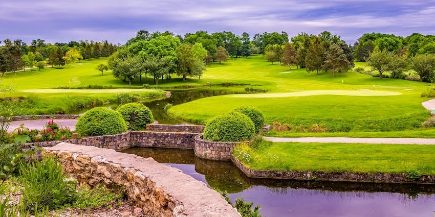 Park with finely cut green grass, plant bushes, a stone bridge over the canal and trees, one of the best things to see in Oregon Ohio.