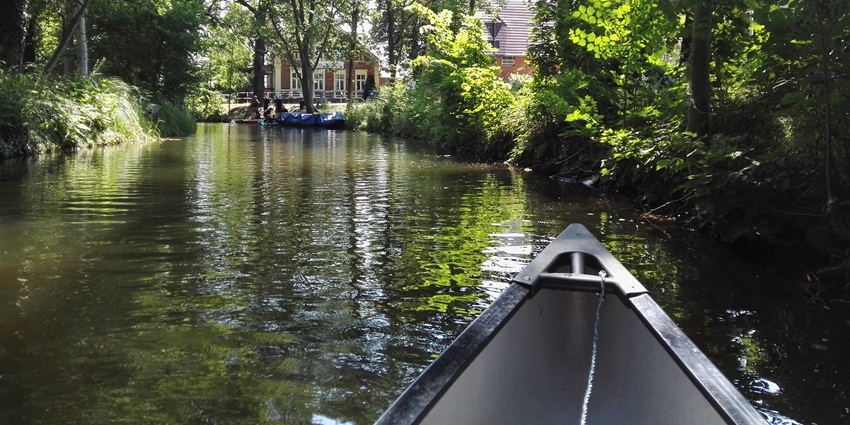 Canoe gliding through a lush green canal, surrounded by trees and riverside cottages, amongst the best places to visit near Berlin.