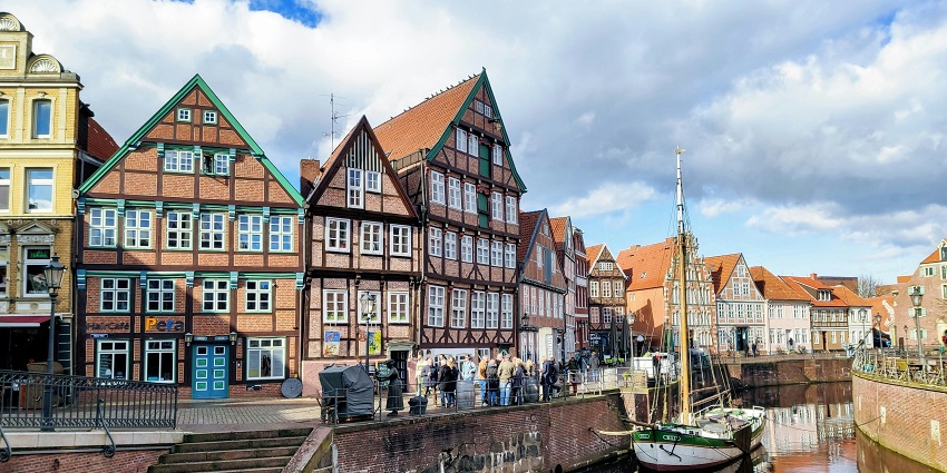 The charming canal-side scene with half-timbered houses, outdoor cafés, and a moored sailboat, one of the places to visit near Hamburg.