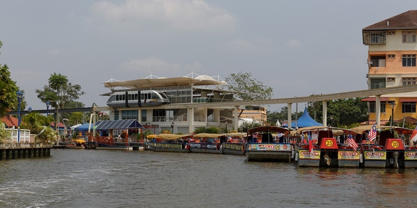 Malacca monorail near the riverbank with cruise boats docked beside colonial buildings, one of the best things to do in Malaysia with family.