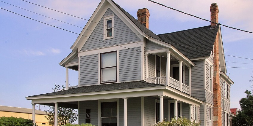 Wide two‑story home with wraparound porch, surrounded by green lawn under blue sky.