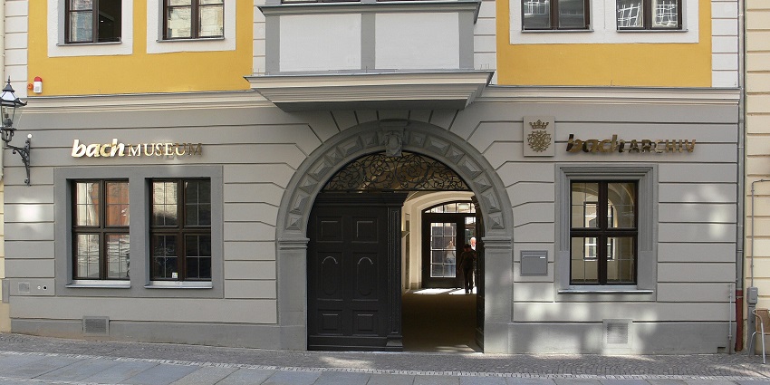 Entrance gate of the Bach Museum in Leipzig with yellow facade and arched doorway.
