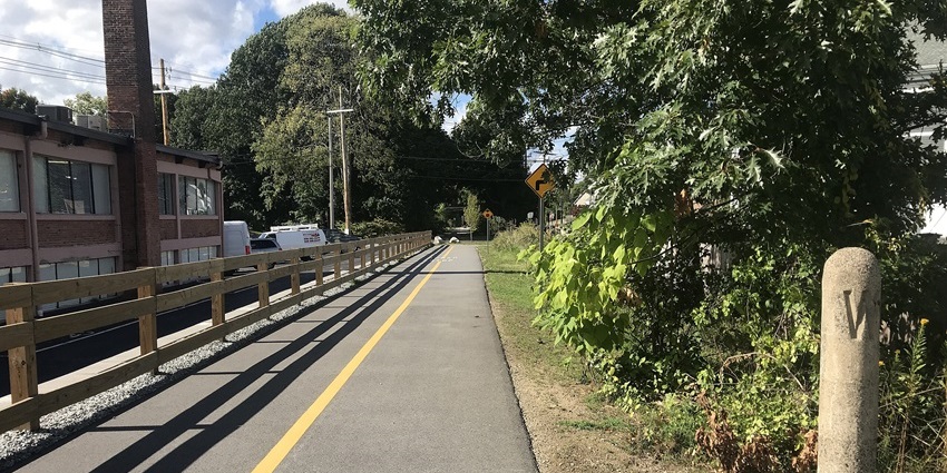 Paved walking and path with yellow line, trees on one side and buildings on the other.