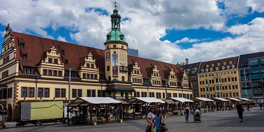 Bustling market square in front of Leipzig’s Old Town Hall with red roof and tower.
