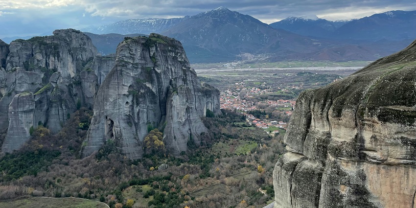 A scenic mountain landscape with rocky peaks and lush greenery with houses at a distance.
