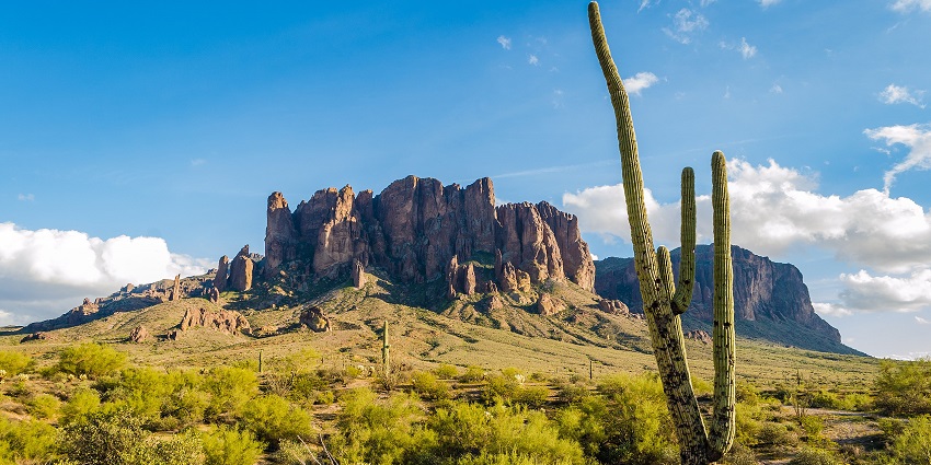 Layered rock formations of the Superstition Mountains towering above sparse green slopes.