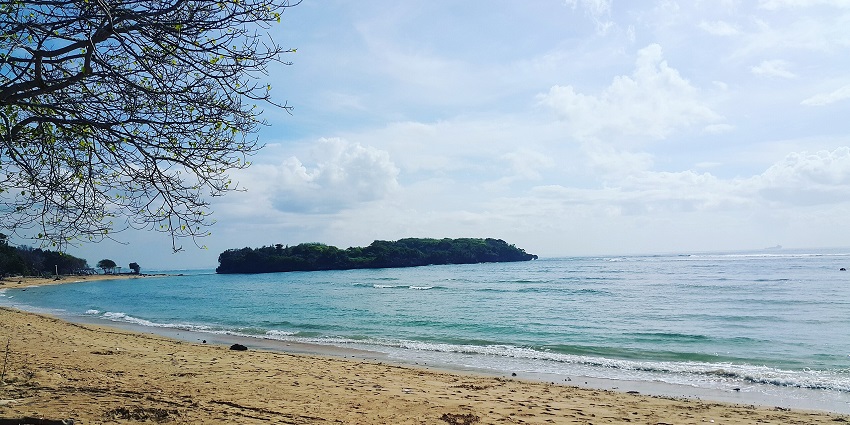 Calm water body at Padang Padang beach with low tide waves, sandy shore and distant greenery.