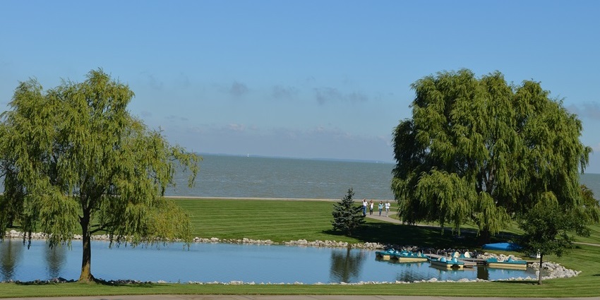 Maumee Bay State Park in Oregon with a lake surrounded by rocks, people walking and green trees.