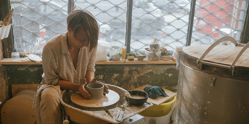 A person in a pottery class moulding clay with a large steel container beside them.