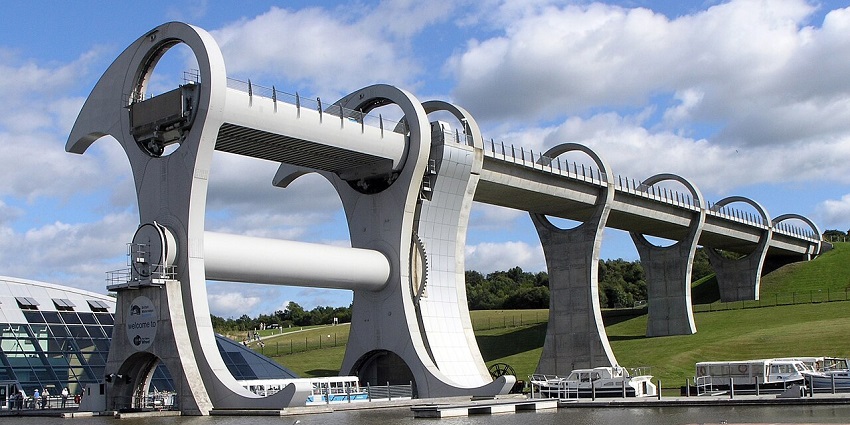 Side view of the Falkirk Wheel, with lush greenery and calm water around the structure.