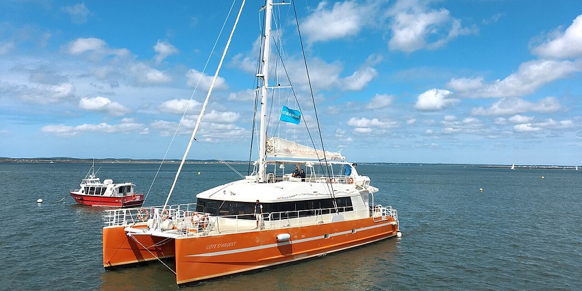 Orange and white Catamaran cruise boat with a distant blue flag and people on the boat.