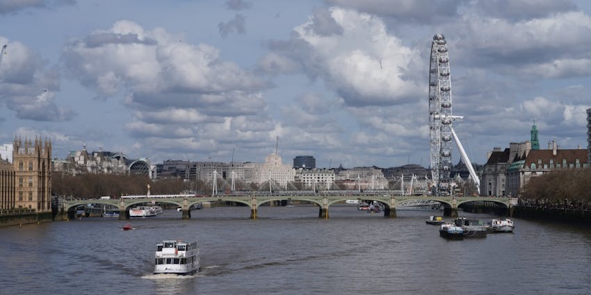 A boat cruising on the Thames River with iconic London landmarks in the background.