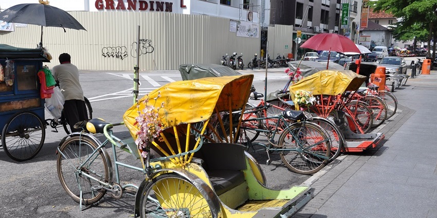 Many decorated trishaws parked on a Penang street near heritage buildings, one of the best things to do in Malaysia with family..