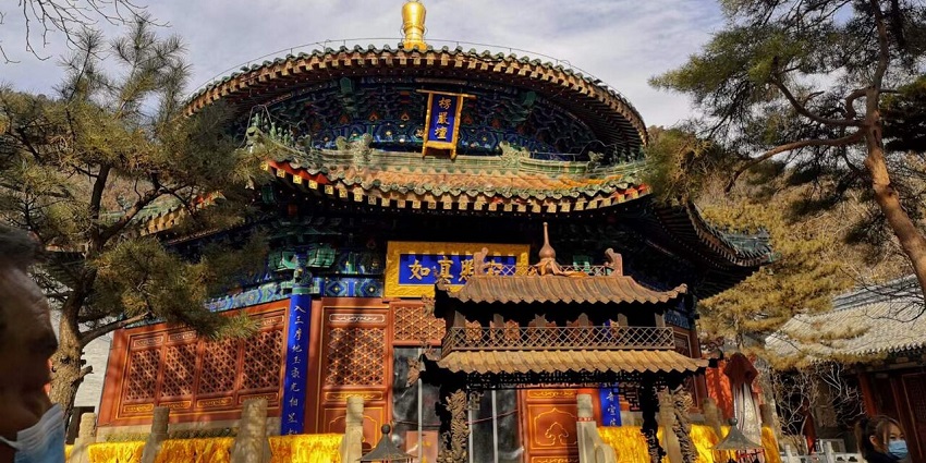Tanzhe Temple is nestled on a lush hillside with traditional rooftops and tall trees around.
