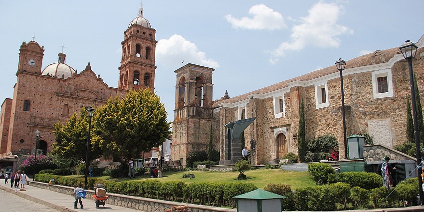 Brick facade of Templo de la Inmaculada Concepción in Tapalpa, set in a tree-lined plaza.