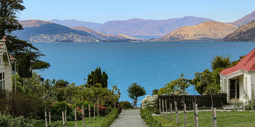 Houses in a farm with a walkway leading to the water body of Lake Te Anau and distant mountains.