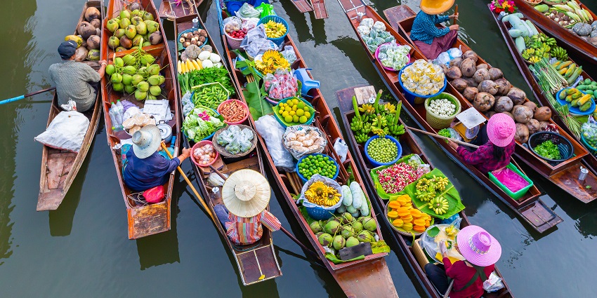 A traditional floating market in Thailand with vendors selling goods from wooden boats on a canal.
