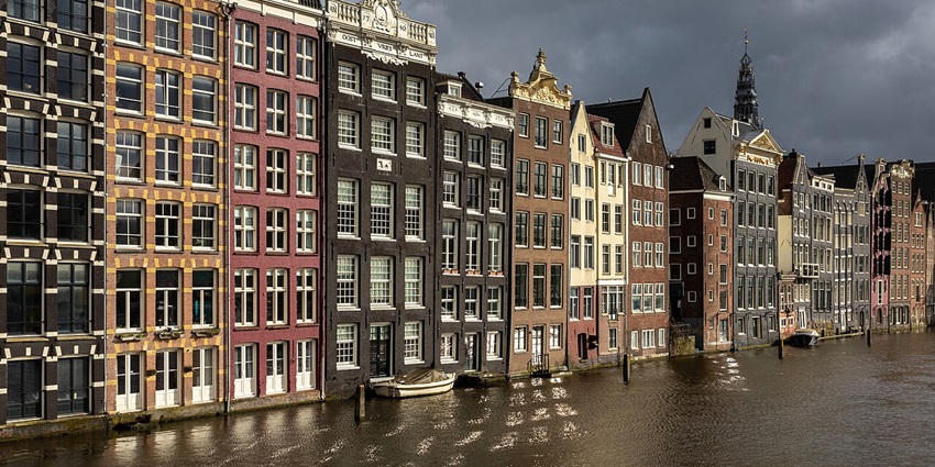 Colourful canal houses along Damrak Avenue in Amsterdam with water reflecting golden hour light.