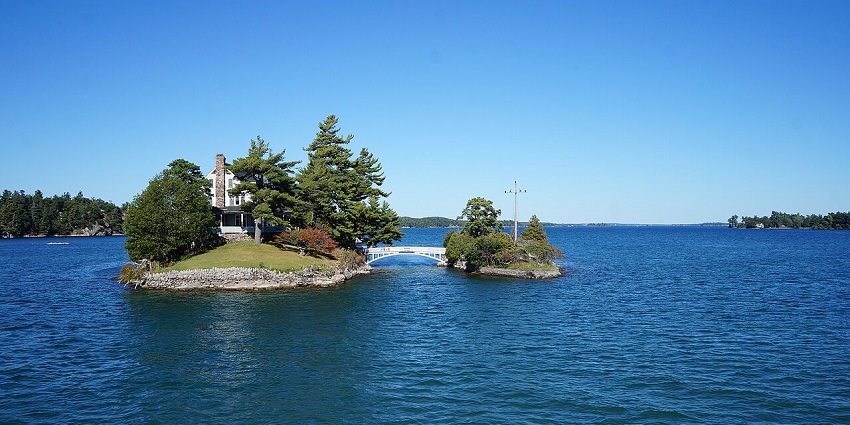 A small cottage sits on the Thousand Islands surrounded by calm waters and lush greenery.