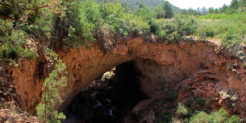 View of Tonto Natural Bridge's rocky arch surrounded by dense greenery and rugged cliffs.
